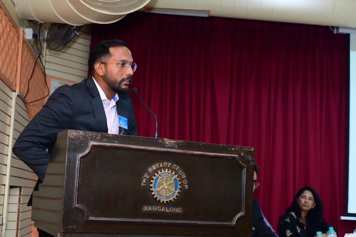Ajay Kanth Gopalam speaking at a Rotary podium in front of red curtains